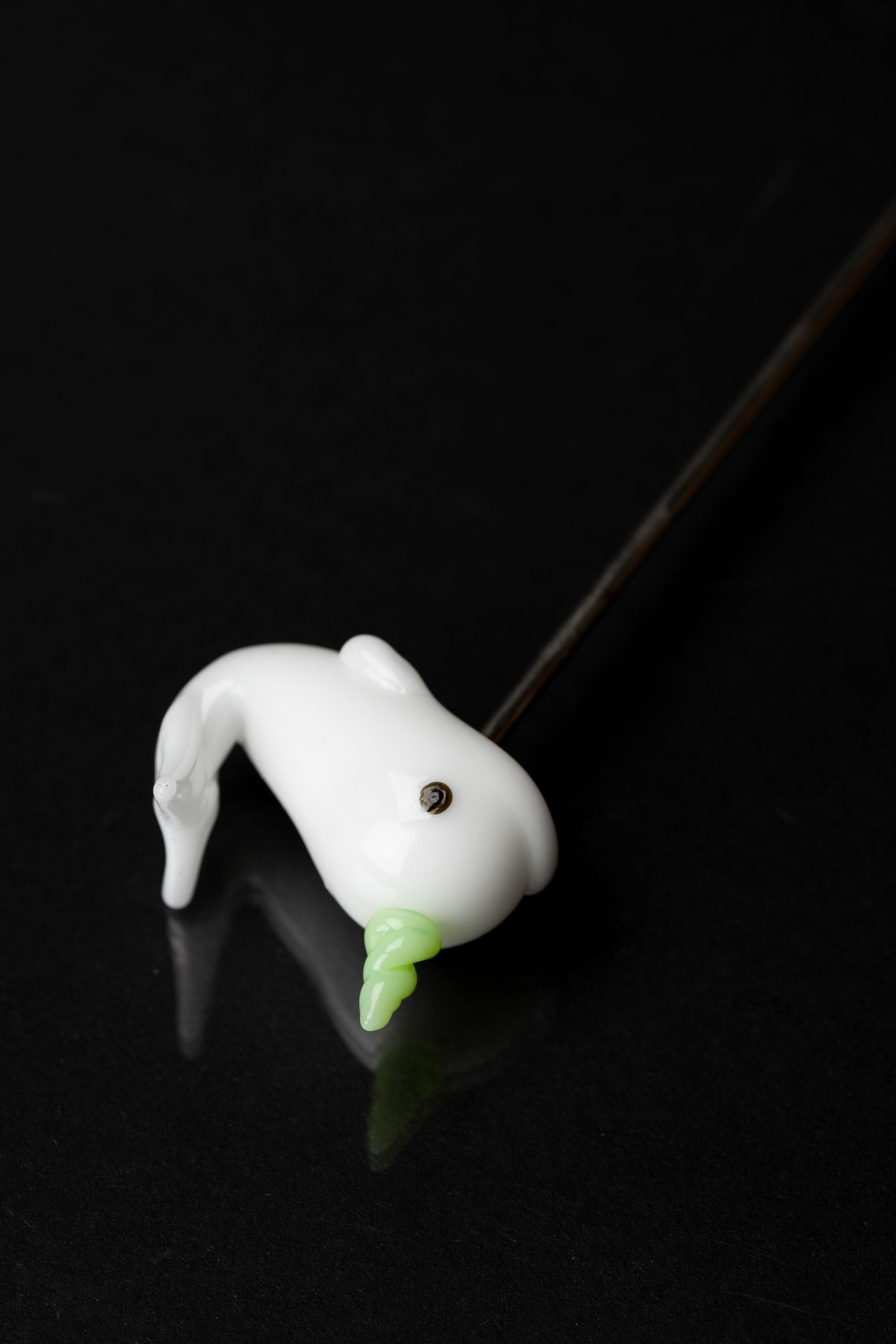Glass cannabis pipe shaped like a ghostly figure with a green tip, isolated on a black background.