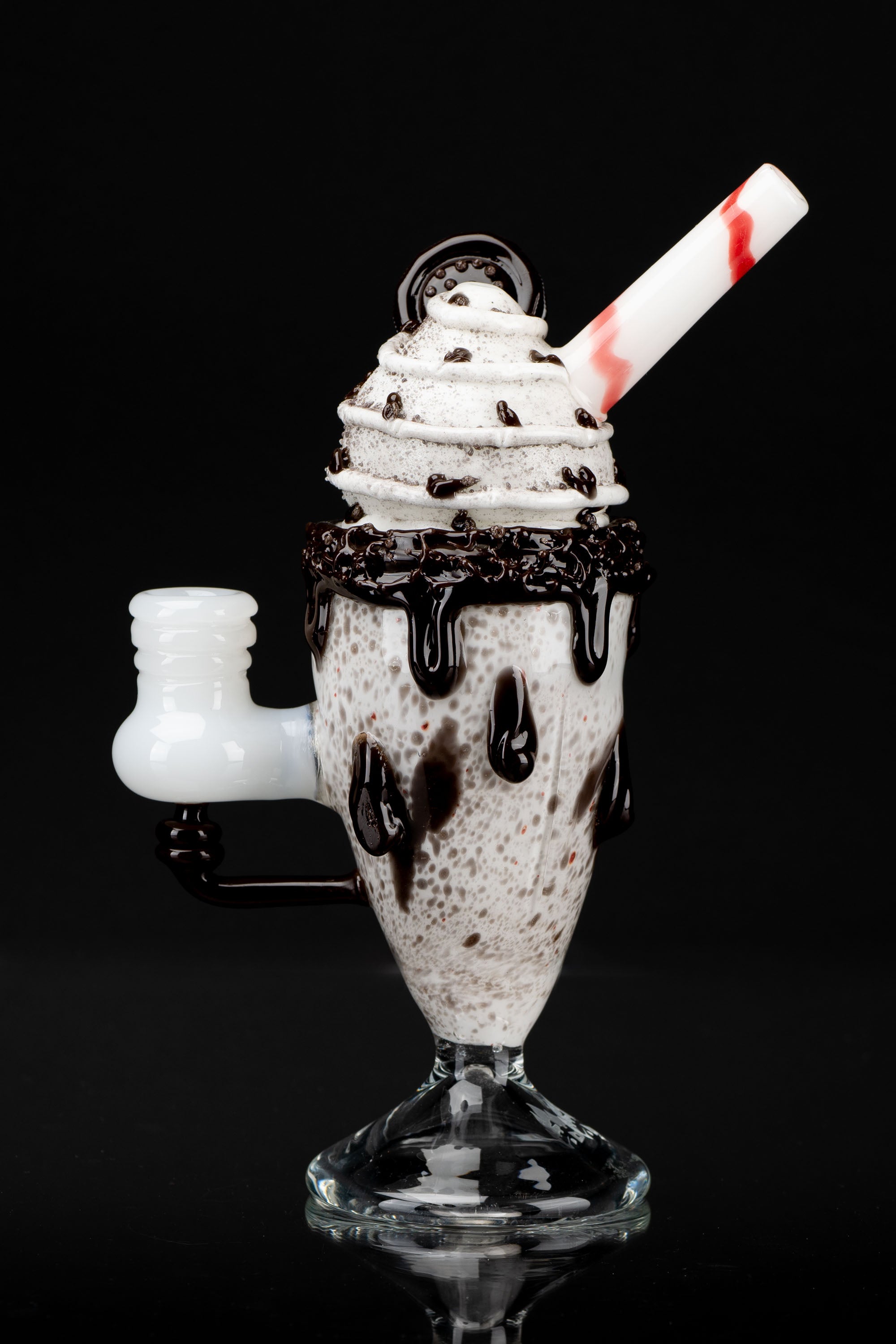 Glass pipe shaped like a chocolate sundae with whipped cream and chocolate drizzle, against a black background.