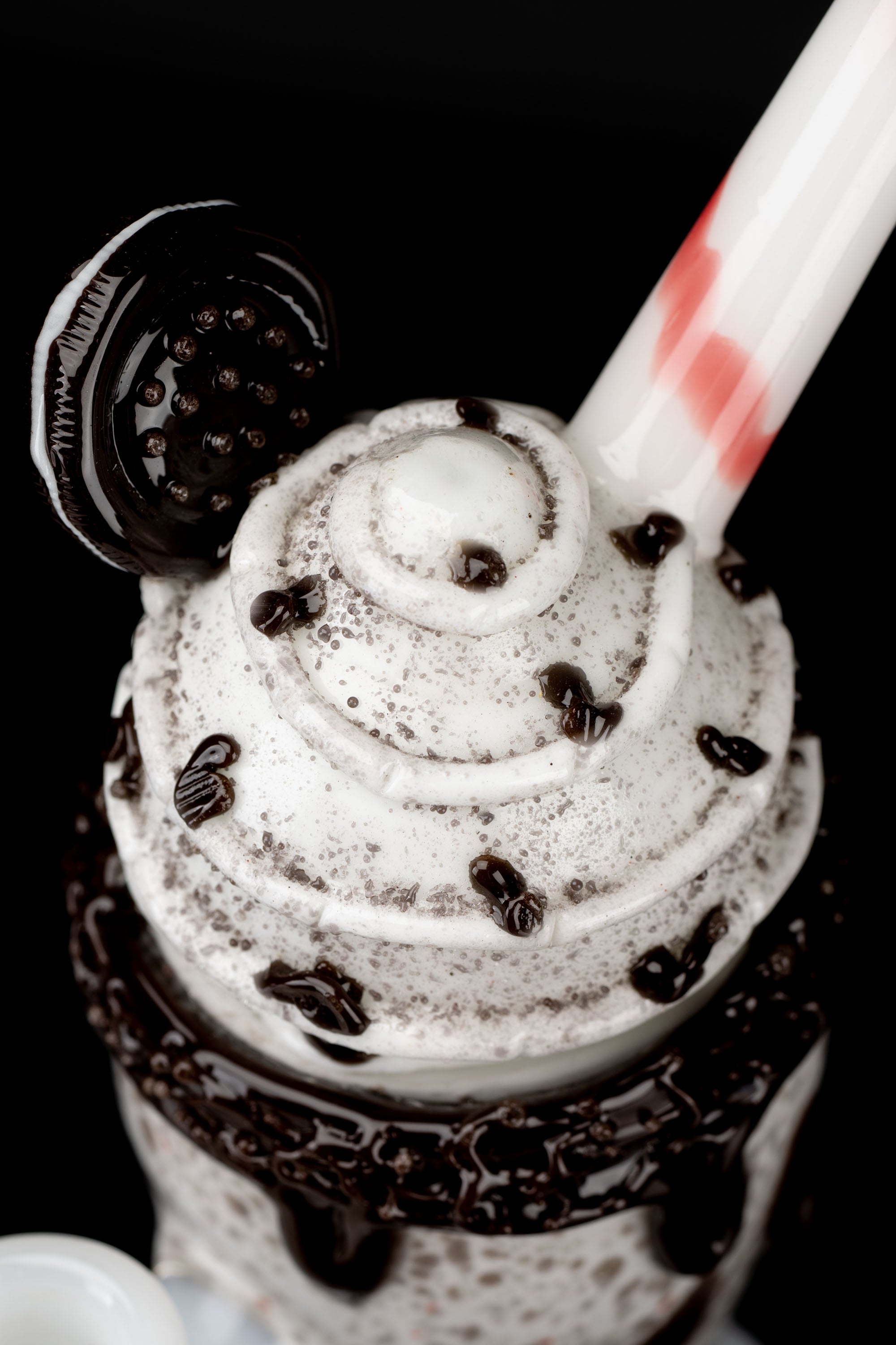 A close-up, top-down view of a chocolate milkshake in a glass, drizzled with chocolate sauce and topped with chocolate chips, alongside a small, dark cannabis accessory.