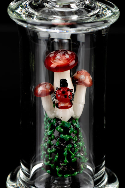 A vibrant glass cannabis pipe sculpted as a cluster of red and white spotted mushrooms with a green base, encased within a clear glass tube.