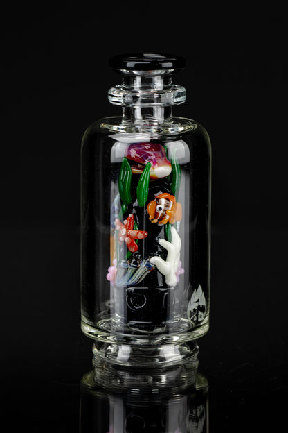 A clear glass bubbler with colorful sculpted glass figures of koi fish and floral elements inside, reflected on a glossy black surface.