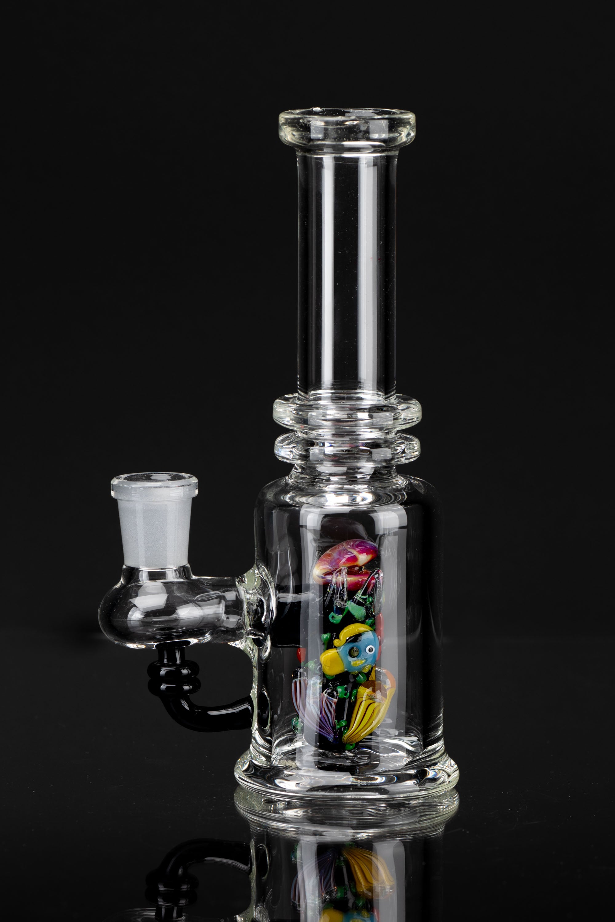 Clear glass water pipe (bong) with colorful glass marbles inside, reflecting on a black surface.