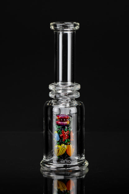 Clear glass bubbler water pipe with colorful glass insects suspended within, reflecting on a dark surface.