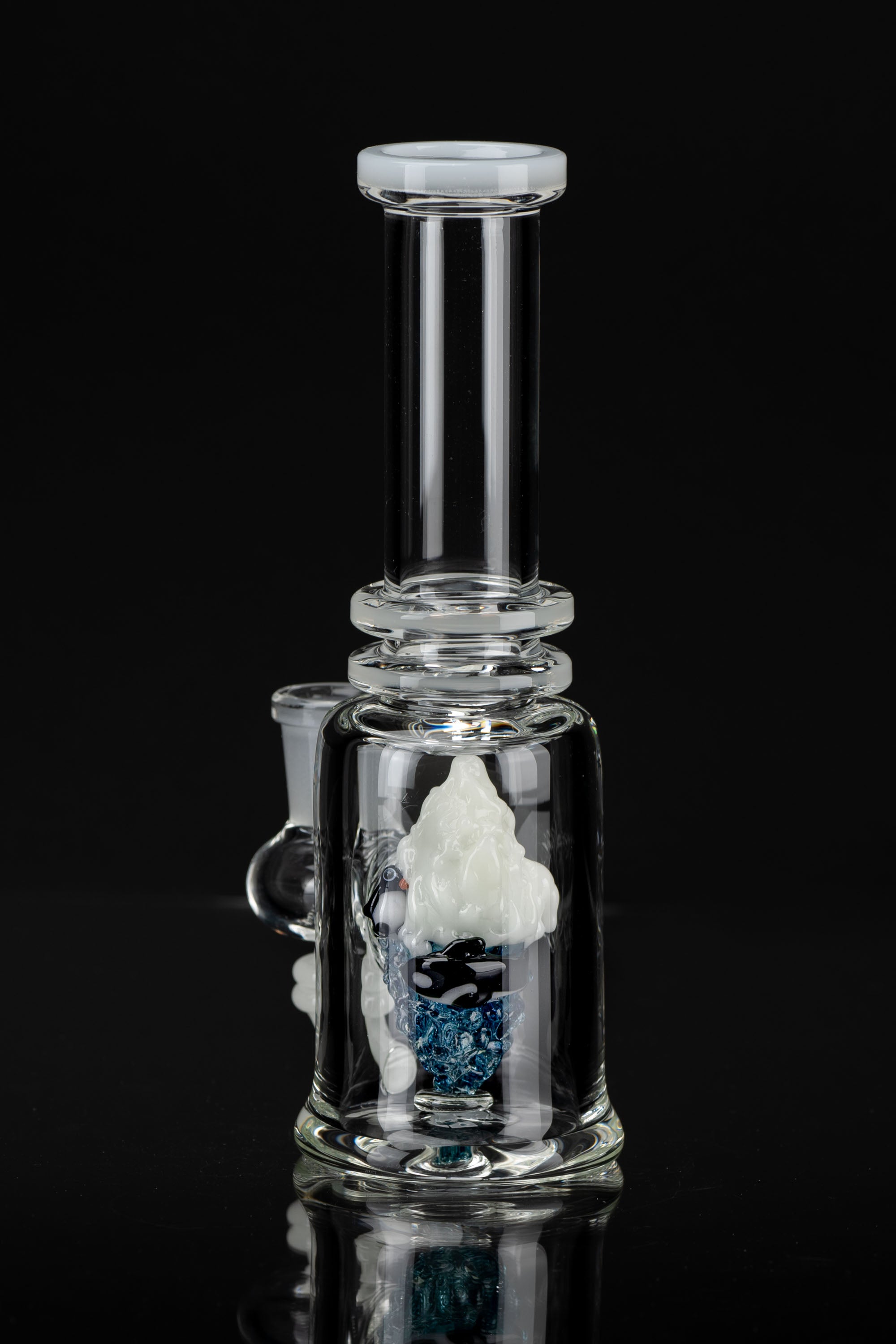 Clear glass bubbler water pipe with sculpted mushroom and blue glitter inside, reflecting on a dark surface.