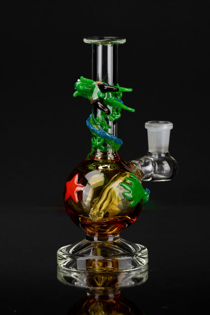 Glass water pipe with colorful sculpted sea life details, reflecting on a black surface.