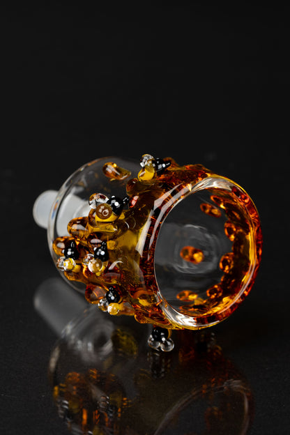 Angled close-up of the Empire Glassworks Bee PuffCo Proxy Attachment showing amber glass bees and droplets on the rim against a black background