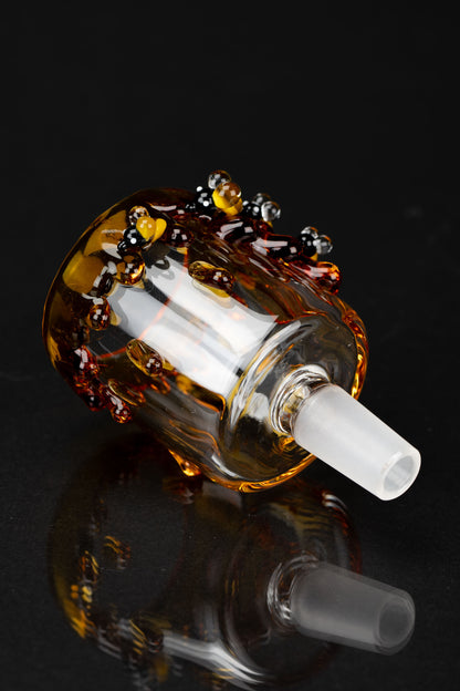 Close-up angled shot of the amber-tinted Empire Glassworks Bee PuffCo Proxy Attachment with bee-dot accents on a black surface