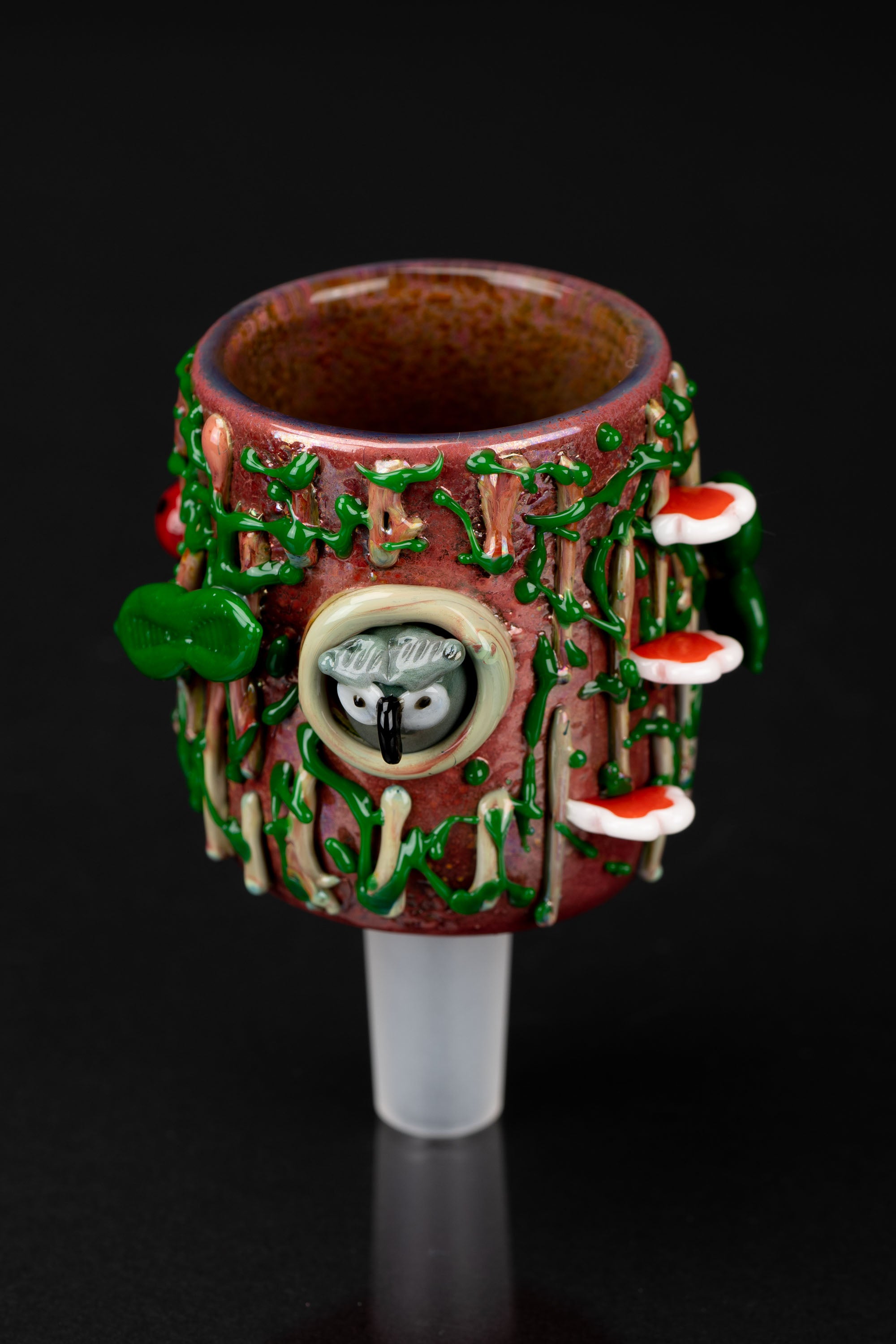 Hand-blown glass cannabis pipe decorated with sculpted mushrooms and a whimsical owl face, against a black background.