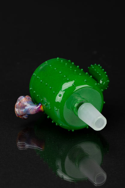 Green glass cactus-shaped water pipe with colorful accents, reflecting on a dark surface.