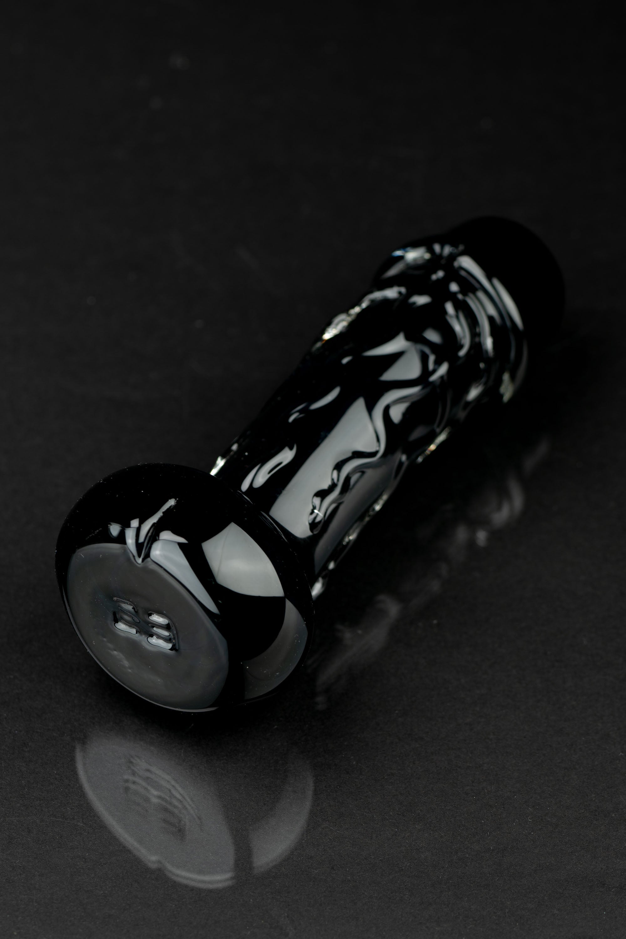 Black glass pipe with intricate white swirls, resting on a reflective surface.