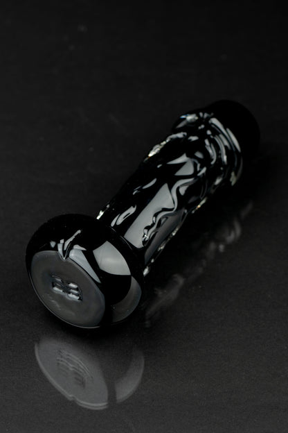 Black glass pipe with intricate white swirls, resting on a reflective surface.