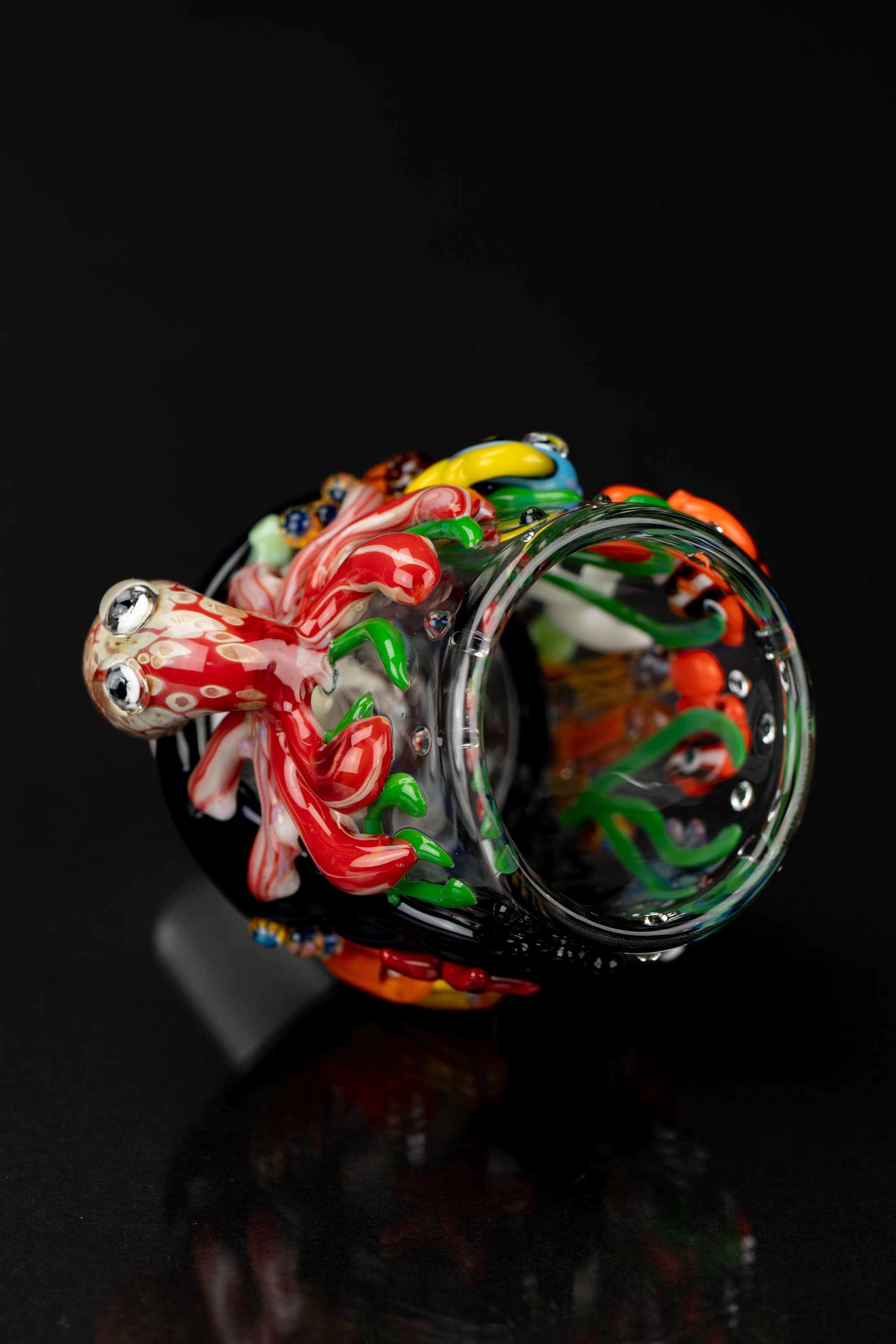Hand-blown glass pipe with colorful, swirling patterns and a sculpted octopus-like mouthpiece, isolated on a black background.