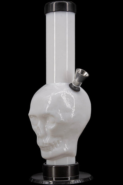 Glass water pipe shaped like a skull with a metal downstem, isolated on black.