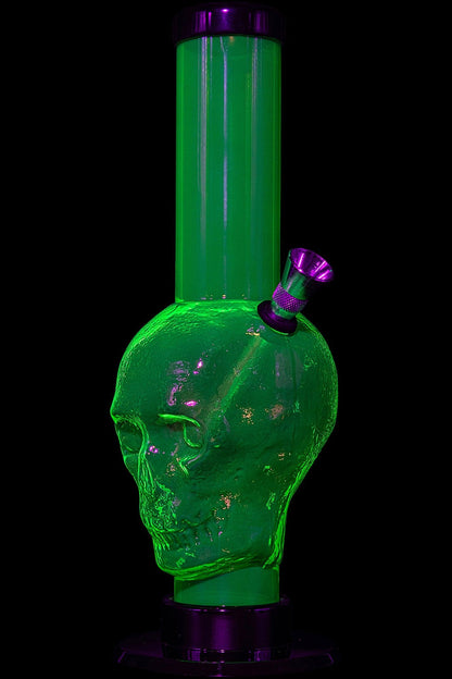 Green glass skull-shaped water pipe with a purple mouthpiece, illuminated in the dark.