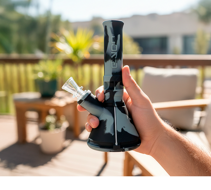 Hand-held, front-angle view of the Jungle Eyce Mini Beaker held outdoors on a sunlit deck, showing its marbled black-and-gray body.