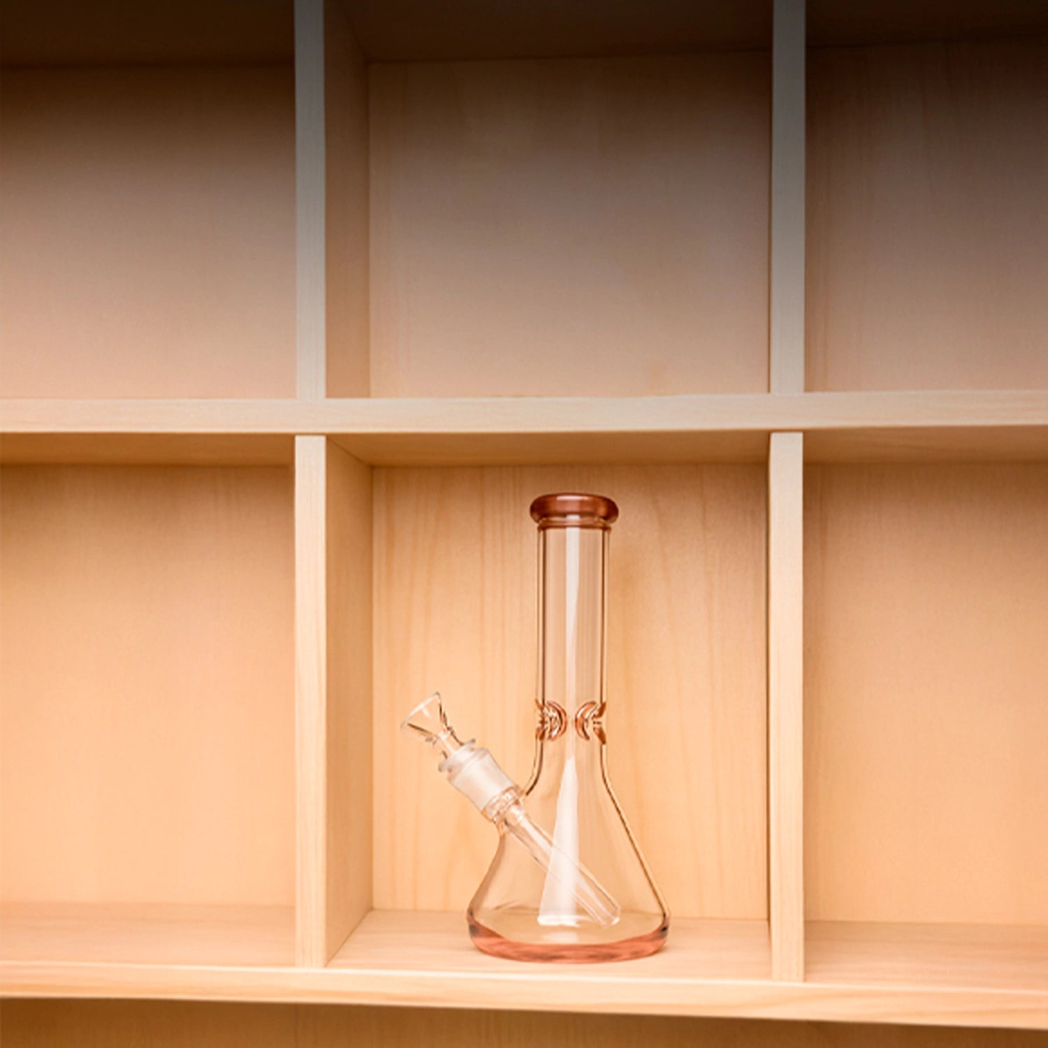 Centered front view of the Smoke Cartel 9mm Big Base Beaker w/ Color Accents Bong - 12 in., shown in transparent black glass on a light wooden cubby shelf.