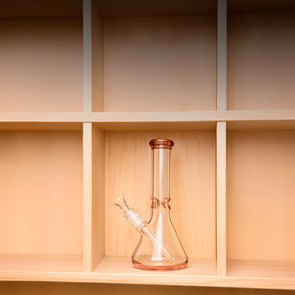 Centered front view of the Smoke Cartel 9mm Big Base Beaker w/ Color Accents Bong - 12 in., shown in transparent black glass on a light wooden cubby shelf.