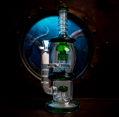 Center-front view of the Smoke Cartel Straight Tube w/ Dual Octopus Perc - 13.5 in. showing clear glass with green accents against a dark porthole-like blue background.