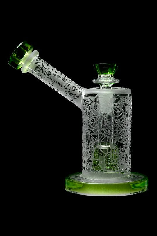 Intricate glass water pipe (bong) with floral carvings, illuminated with green light against a black background.