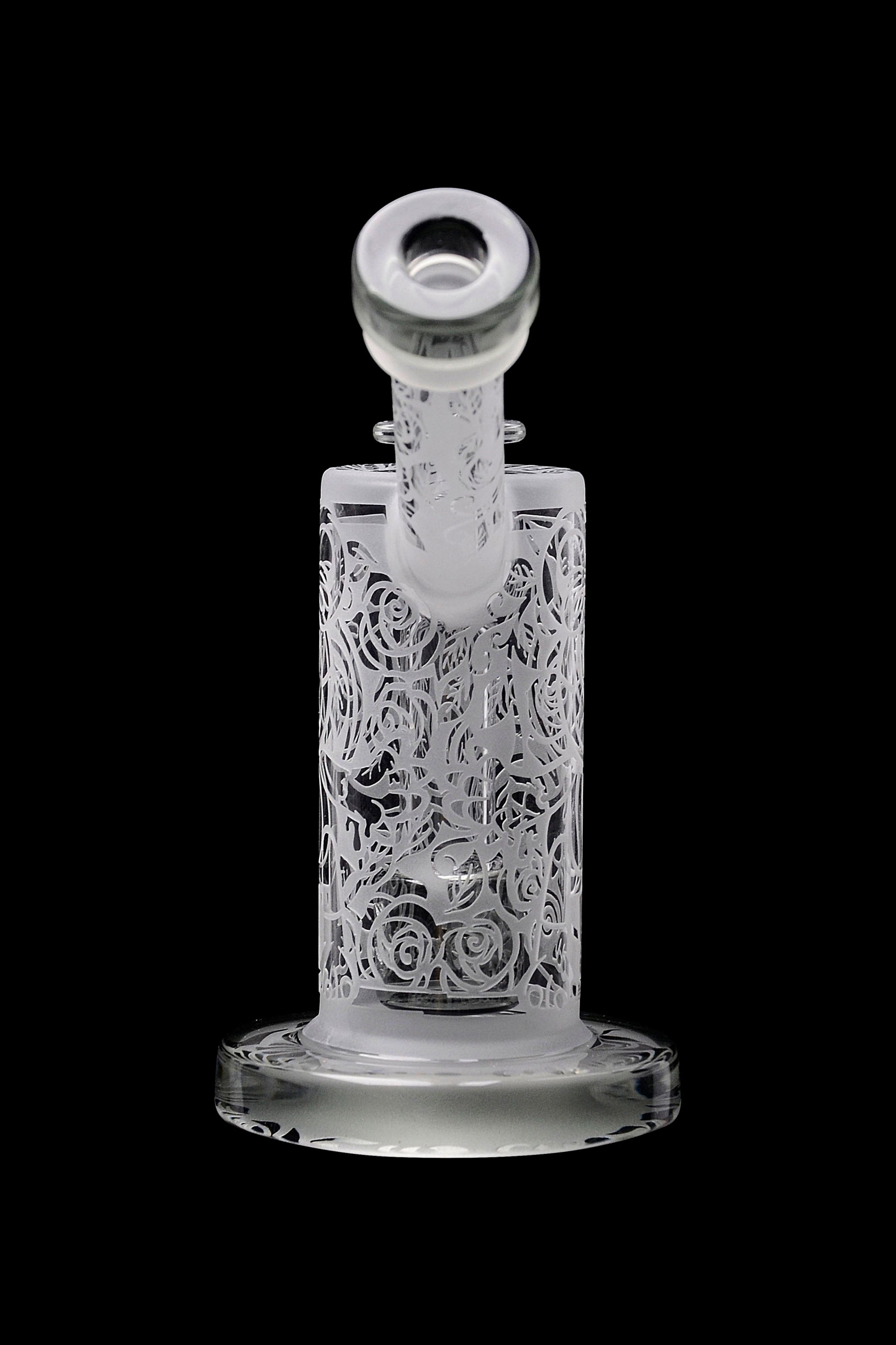Clear glass water pipe with intricate rose carvings, isolated on a black background.
