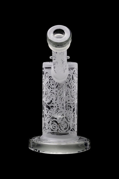 Clear glass water pipe with intricate rose carvings, isolated on a black background.