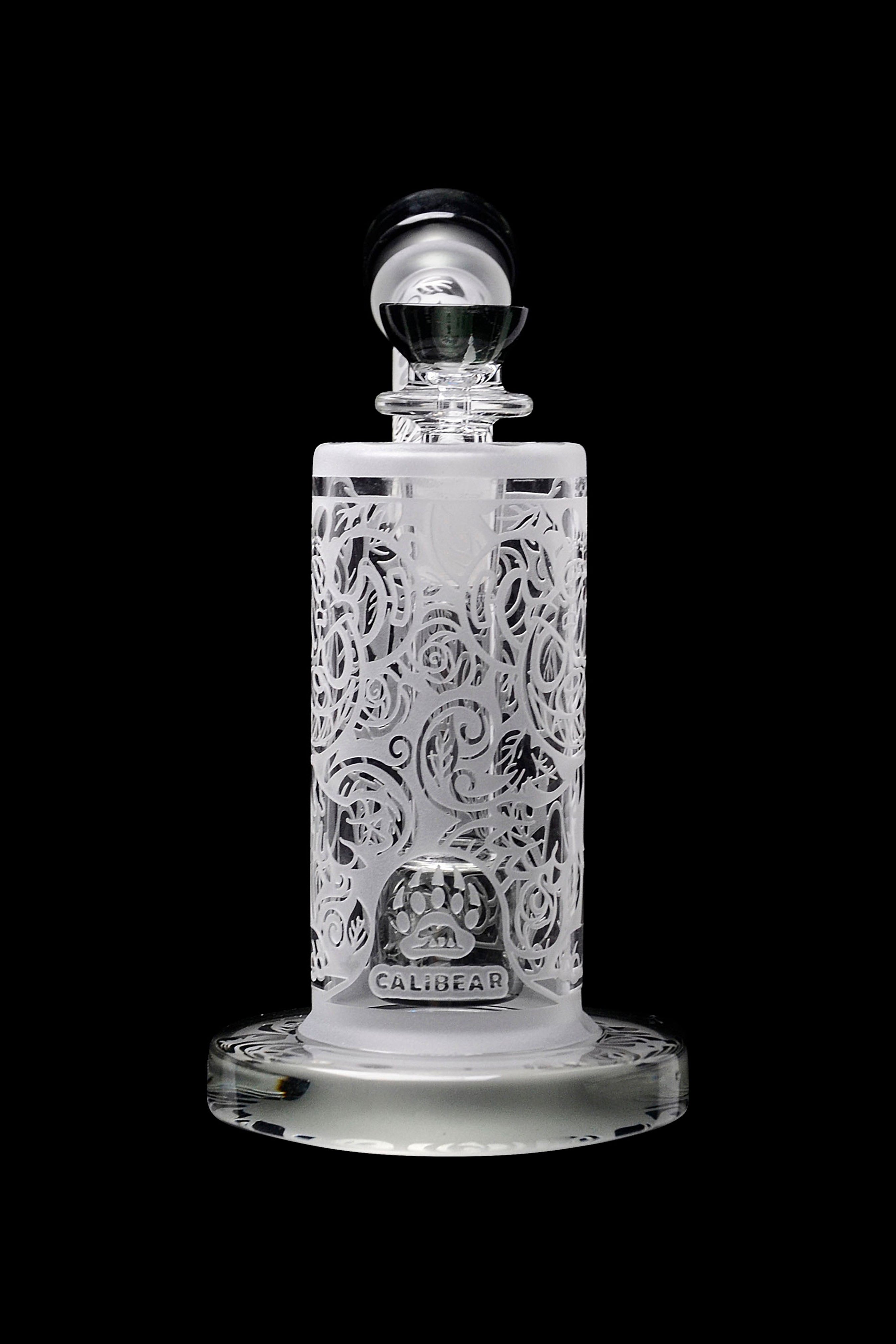 Clear glass cannabis oil concentrate container with intricate floral carving and “Calibear” branding.