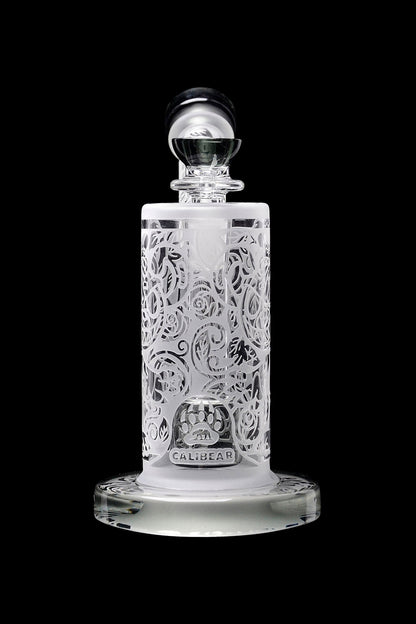 Intricate glass cannabis oil rig with ornate floral carvings and a branded base.