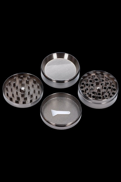 Metal cannabis grinder disassembled into its component parts on a black background.