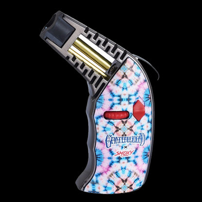 Angled close-up of the Grateful Dead Thrust Torch showing its open nozzle, exposed brass fuel tube, and tie-dye patterned handle with red control buttons against a black background