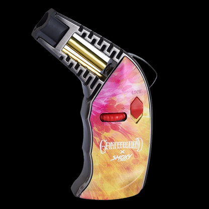 Angled close-up of the Grateful Dead Thrust Torch showing its pink-yellow patterned body, red control wheel and exposed gold ignition tube against a black background