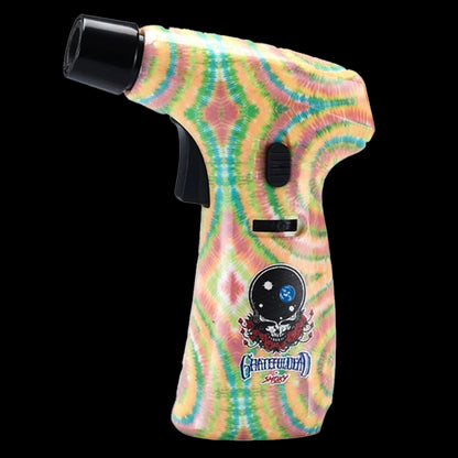 Angled close-up of the Grateful Dead Power Torch showing its yellow‑green tie‑dye body, black nozzle and trigger, and skull logo on a black background