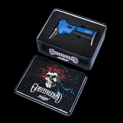Angled top-down view of the blue Grateful Dead Torch Deluxe nestled in black foam inside a tin with skull-and-roses lid art.