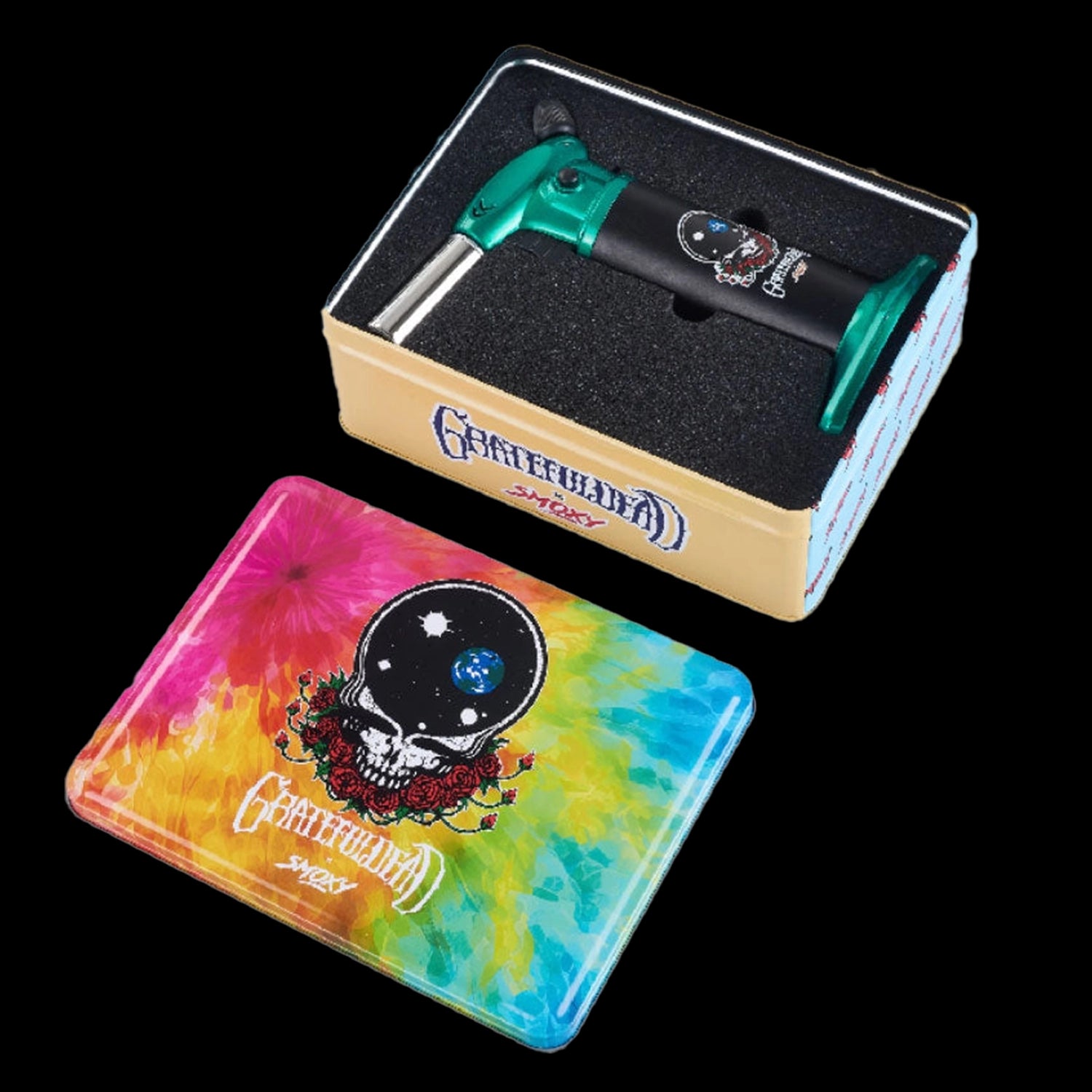 Angled top view of the Grateful Dead Vulcan Torch nestled in black foam inside a tan box beside a tie-dye skull tin.
