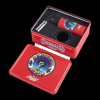 Angled top-down view of a red Grateful Dead Dragon Torch nestled in its foam-lined red tin, showing the torch's skull-and-rose logo.