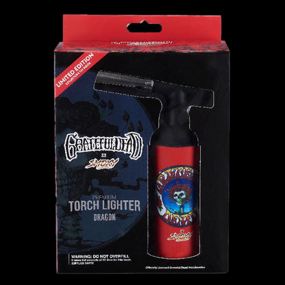 Front-facing shot of the Grateful Dead Dragon Torch boxed in black and red packaging showing the red torch lighter with a skull-and-rose emblem visible through a die-cut window.