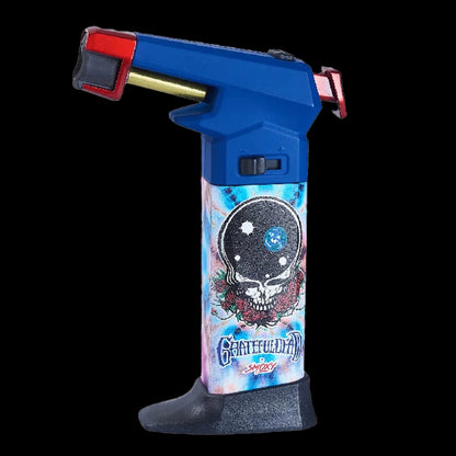 Close-up side view of the Grateful Dead The Rock Torch showing a blue top, brass nozzle and a tie-dye body with the Grateful Dead skull and roses motif.