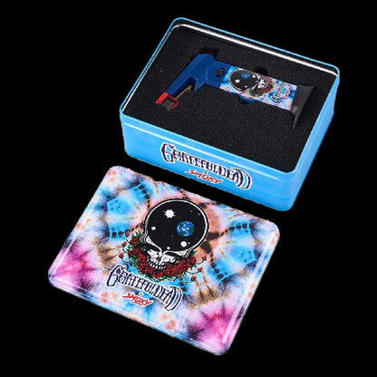 Angled top view of the Grateful Dead The Rock Torch in blue nestled in black foam inside a matching blue tin above a tie-dye pad.
