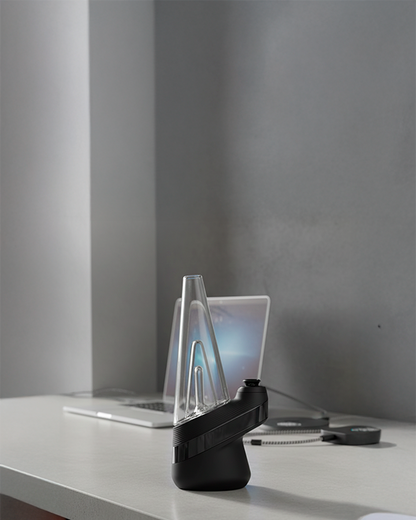 Side view of the LA Pipes 5mm Thick Beaker Bong with Showerhead Perc sitting on a desk in front of a laptop, backlit by soft gray wall light.