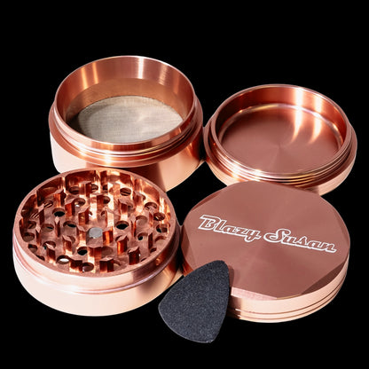 Close-up top-down view of the rose gold Blazy Susan 4-pc 3 Chamber Grinder showing its four separated pieces, grinding teeth, mesh screen, and branded lid.