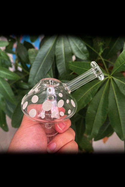A hand holding a patterned glass bubbler with a green plant background.