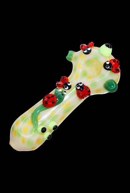 Angled close-up of the Smoke Cartel Fancy Ladybug and Snail Spoon Pipe - 6 in., a pale green glass spoon decorated with red ladybugs and raised green snail accents on a black background
