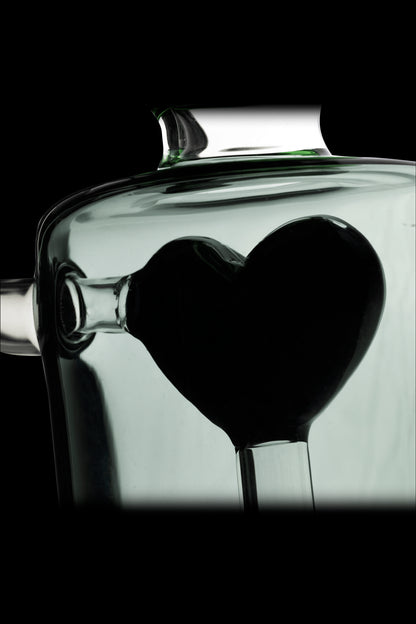 A glass cannabis water pipe shaped like a heart, silhouetted against a pale green background.