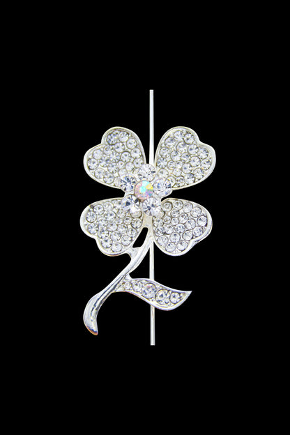 A close-up of a jeweled, four-leaf clover-shaped cannabis pipe against a black background.