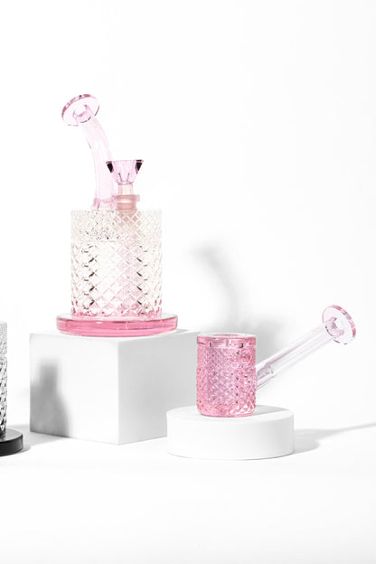 Pink glass cannabis rig and accompanying piece displayed on white pedestals.