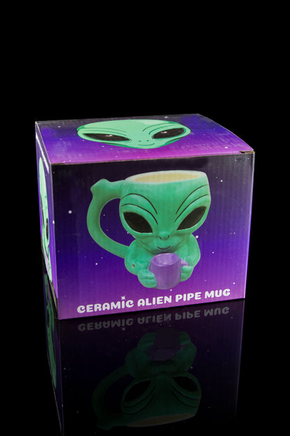 A vibrant purple ceramic alien-shaped pipe mug sits atop a matching box with mirrored text, presented against a dark background.