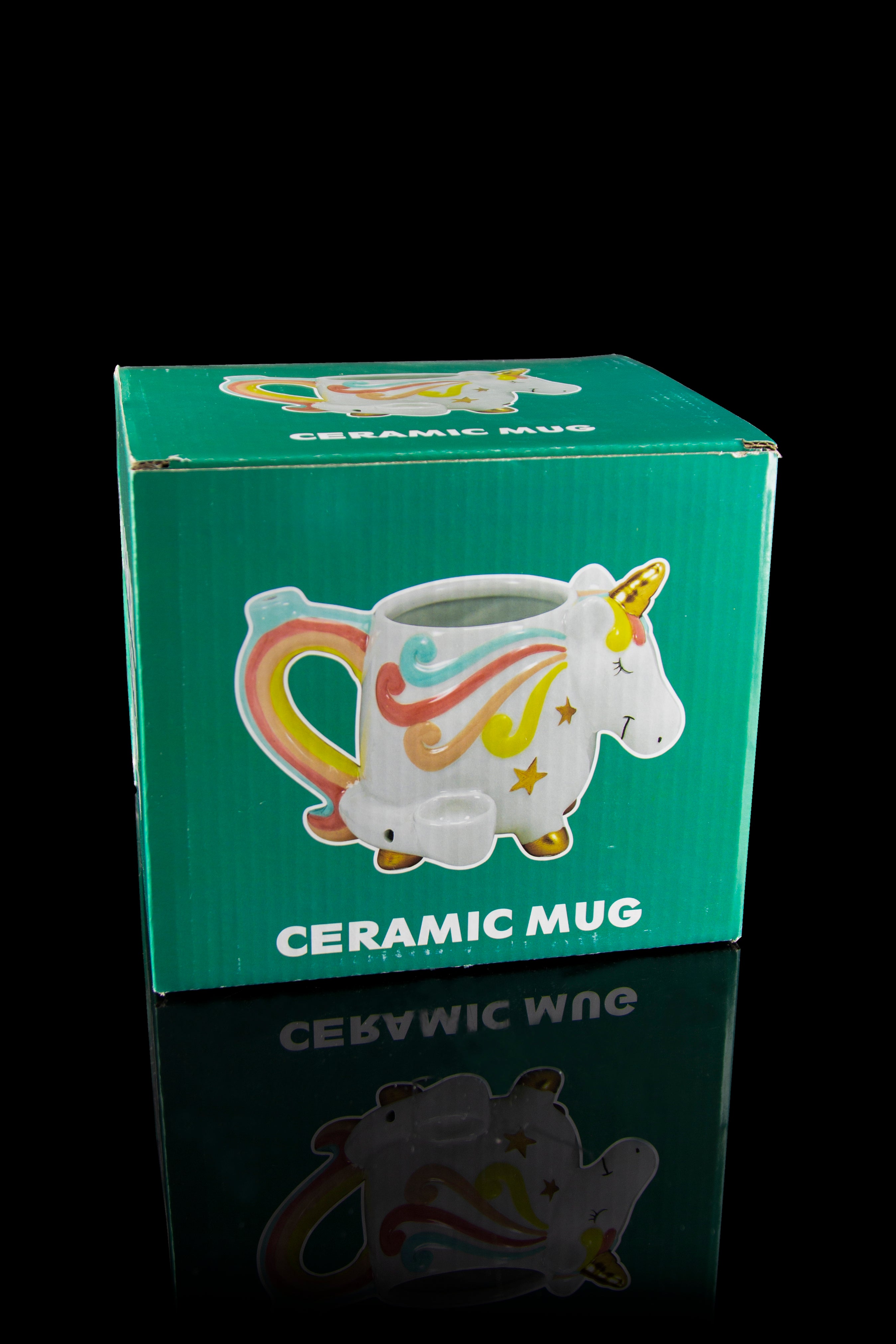 Unicorn-shaped ceramic mug in a green box, reflected on a glossy surface."