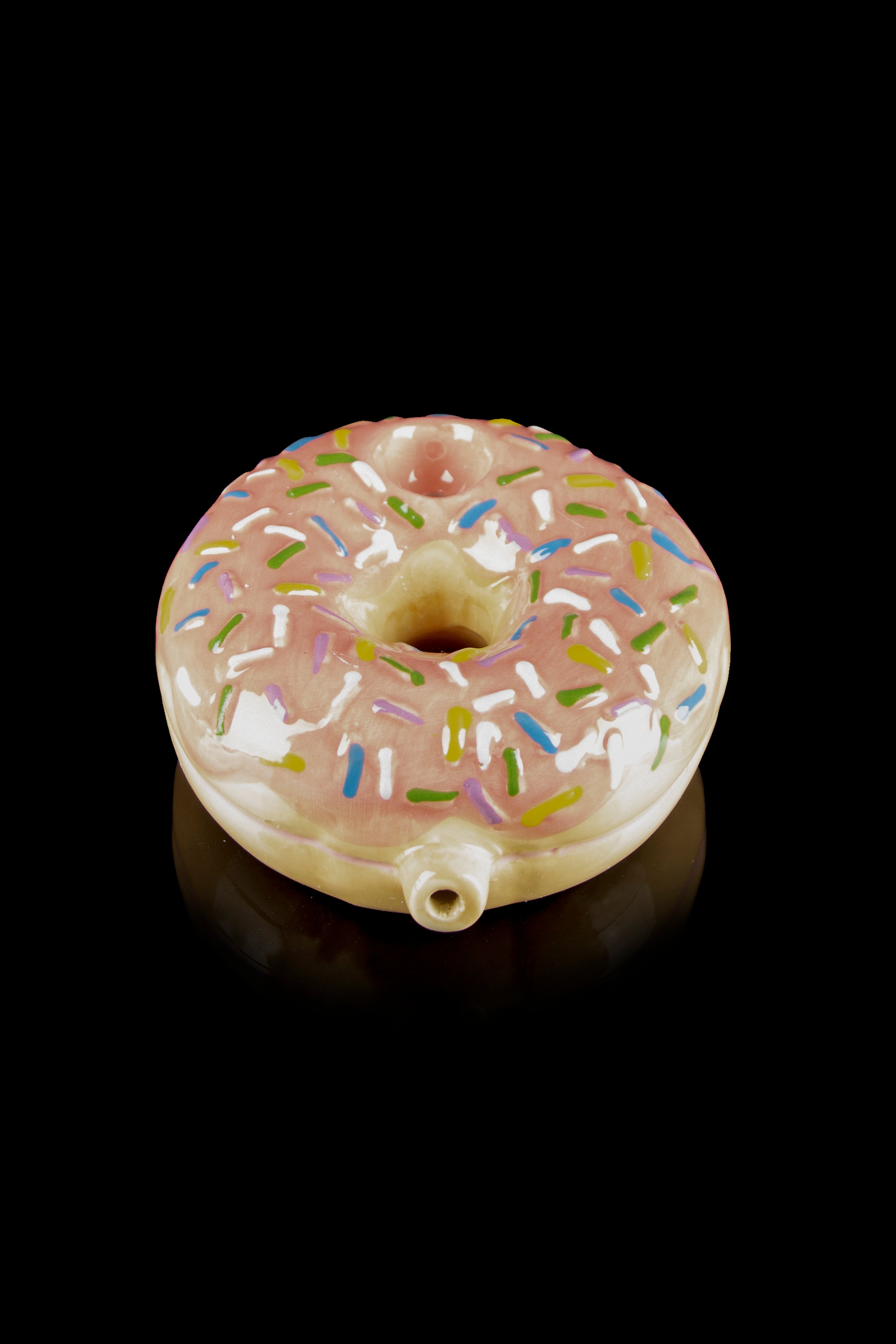 Glass donut-shaped smoking pipe with pink frosting and colorful sprinkles, isolated on a black background.