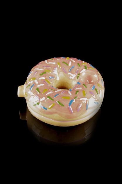 Pink glazed donut-shaped glass pipe with colorful sprinkles, reflecting on a black surface.
