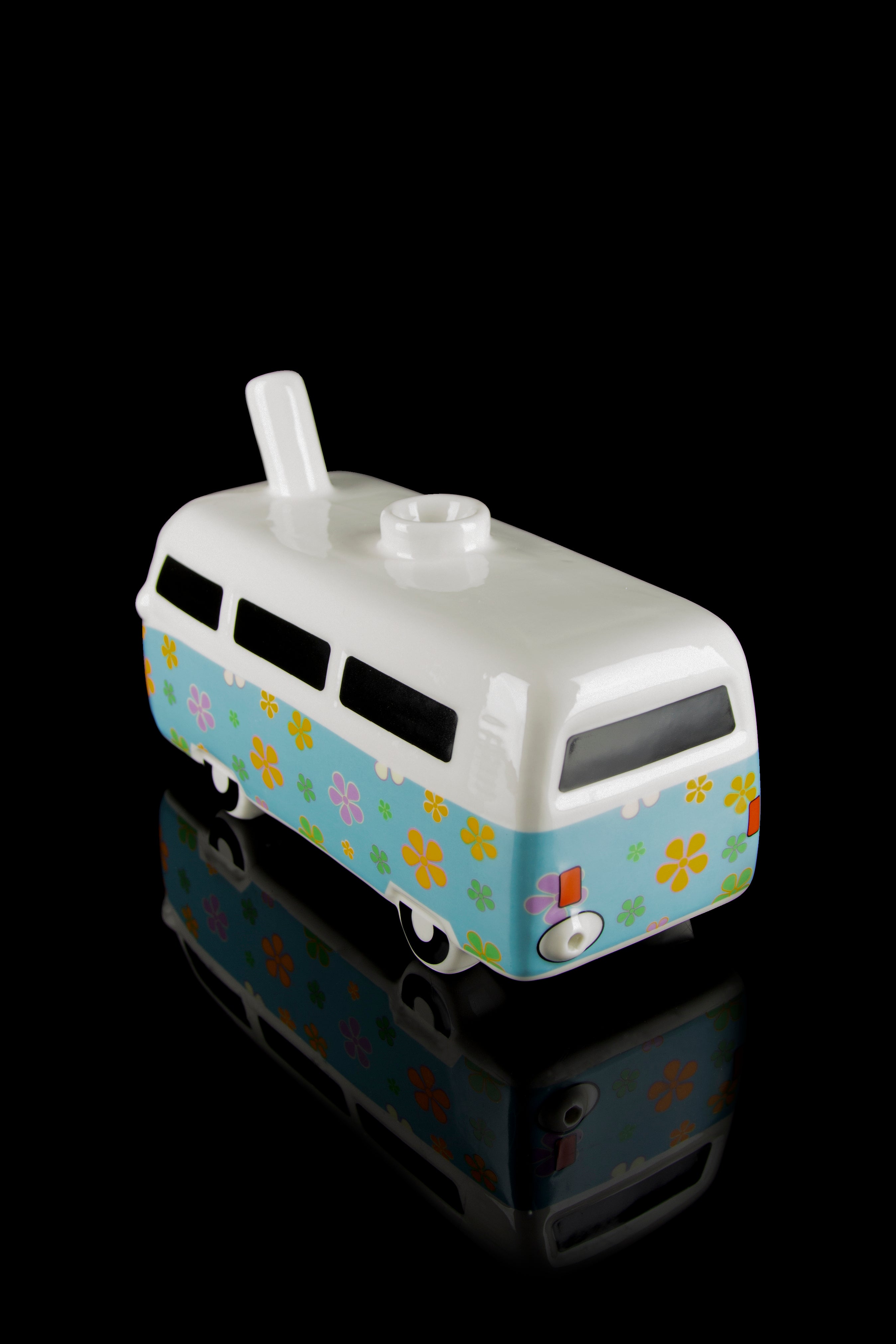 A colorful glass water pipe shaped like a vintage VW van with a floral pattern, displayed on a reflective black surface.