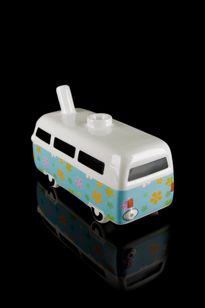 A colorful glass water pipe shaped like a vintage VW van with a floral pattern, displayed on a reflective black surface.